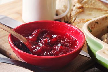 The world's easiest cranberry sauce in a red bowl next to a casserole dish, with roast turkey and a gravy pitcher in the background.