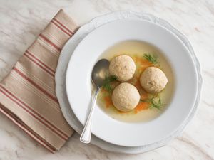 Overhead view of matzo ball soup served in a shallow white bowl, garnished with dill sprigs.