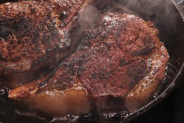 Two dry-aged steaks cooking in a cast iron skillet.