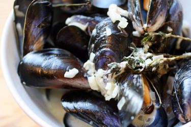 A close-up of mussels just cooked in their shells, with Roquefort cheese and sprigs of fresh thyme