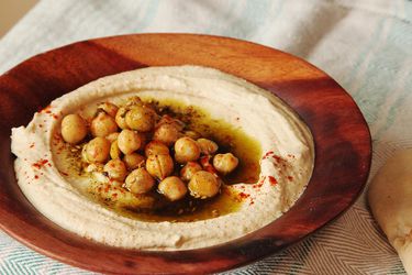 以色列式鹰嘴豆泥，盛在浅木碗里，浇上煮好的鹰嘴豆、橄榄油、扎塔尔和辣椒粉。gydF4y2Ba