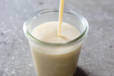 Stream of homemade sweetened condensed milk being poured into glass jar