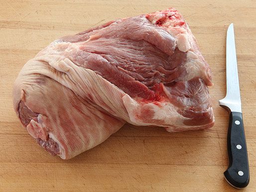 未煮熟的猪肩放在砧板上，旁边是一把刀。