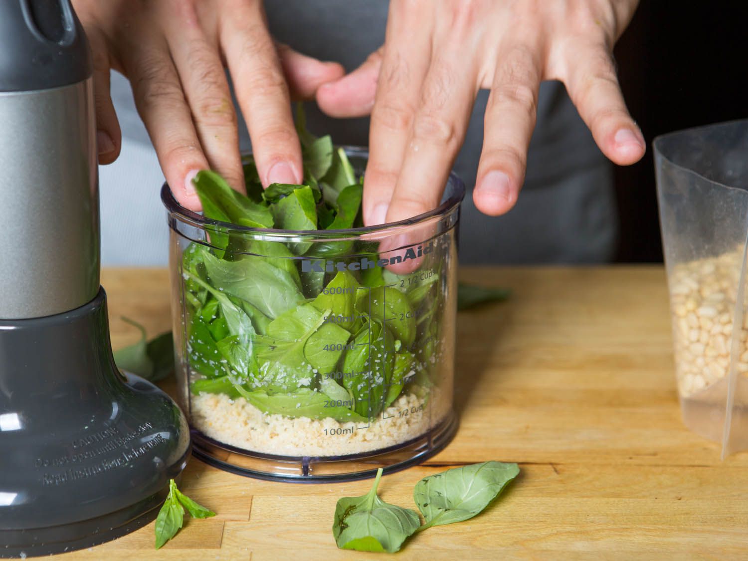 Basil being added to pine nut and garlic purée in food processor