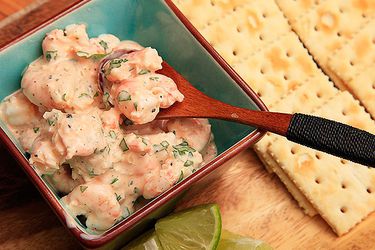 Spooning up Colombian shrimp cocktail in a bowl with saltine crackers and lime wedges on the side