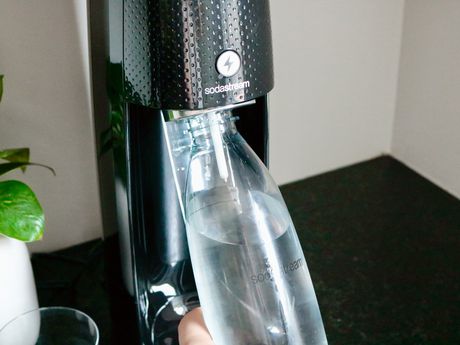 a hand inserting a plastic soda maker bottle into the machine