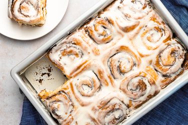Cinnamon rolls in pan with a roll served on a plate peeking into frame