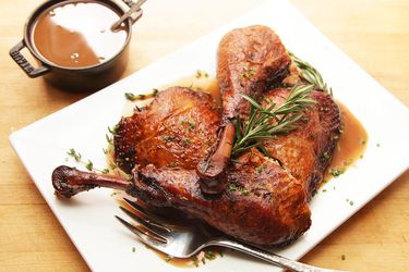 Overhead view of red wine-braised turkey legs on a white plate next to a pot of gravy.