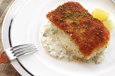 A piece of pan-seared fish with a crispy crumb coating on top, sprinkled with chopped herbs.
