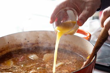 an oxo mini measuring cup being used to pour liquid into a pot of cooking stew