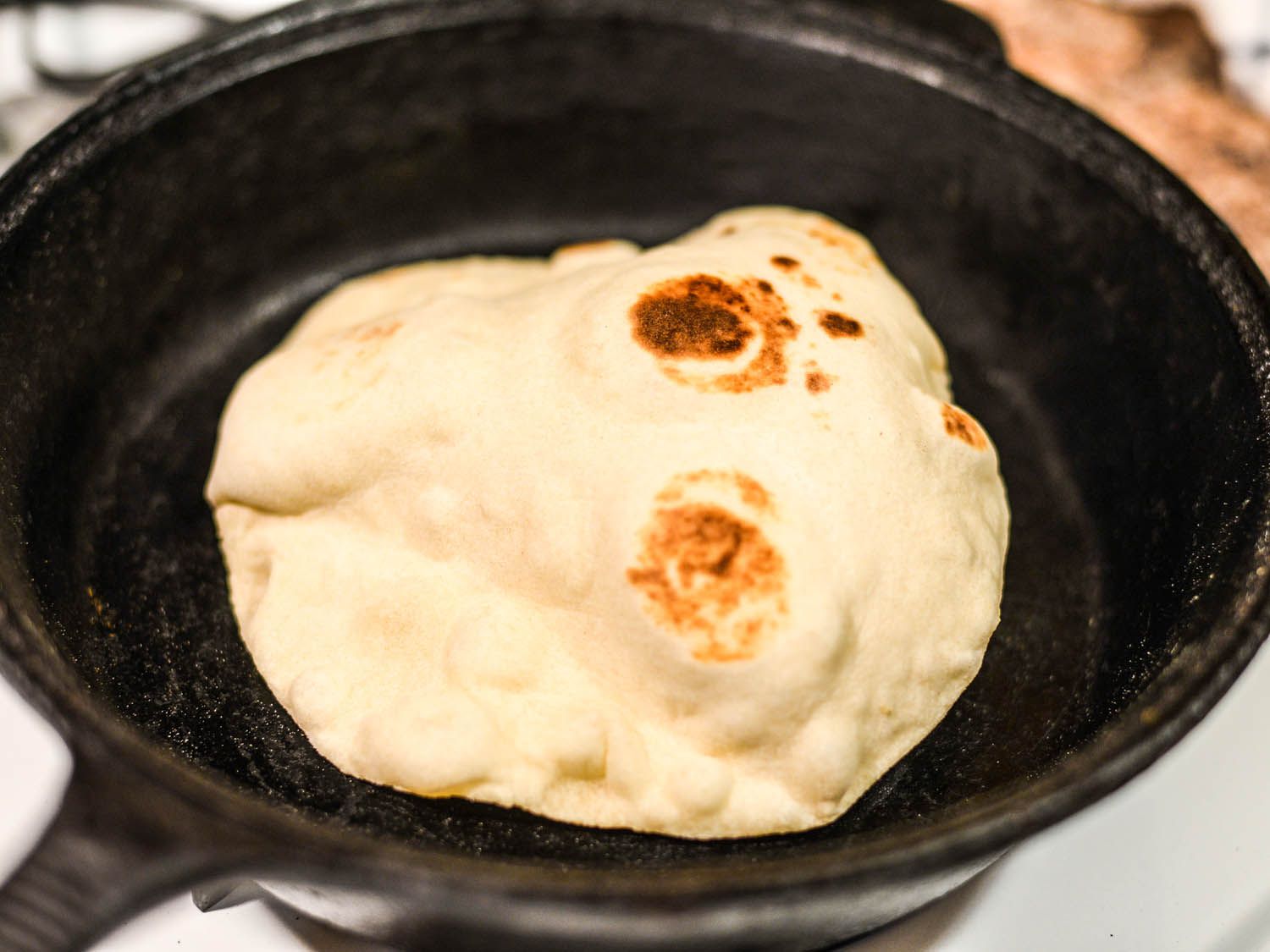 在铸铁煎锅里，有烧焦斑点的玉米粉圆饼在膨胀。