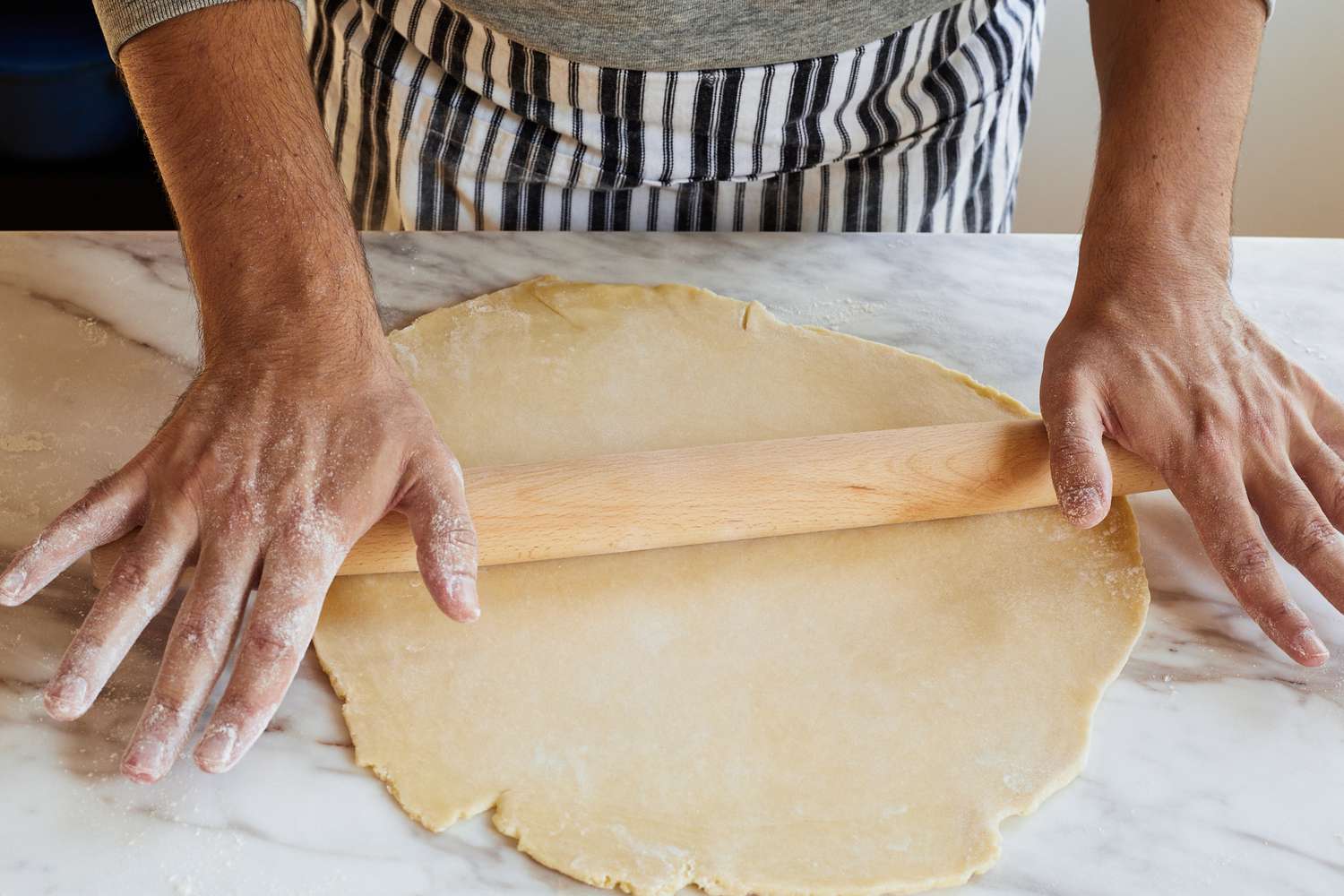 两只手使用锥形擀面杖推出pie crust on a marble surface