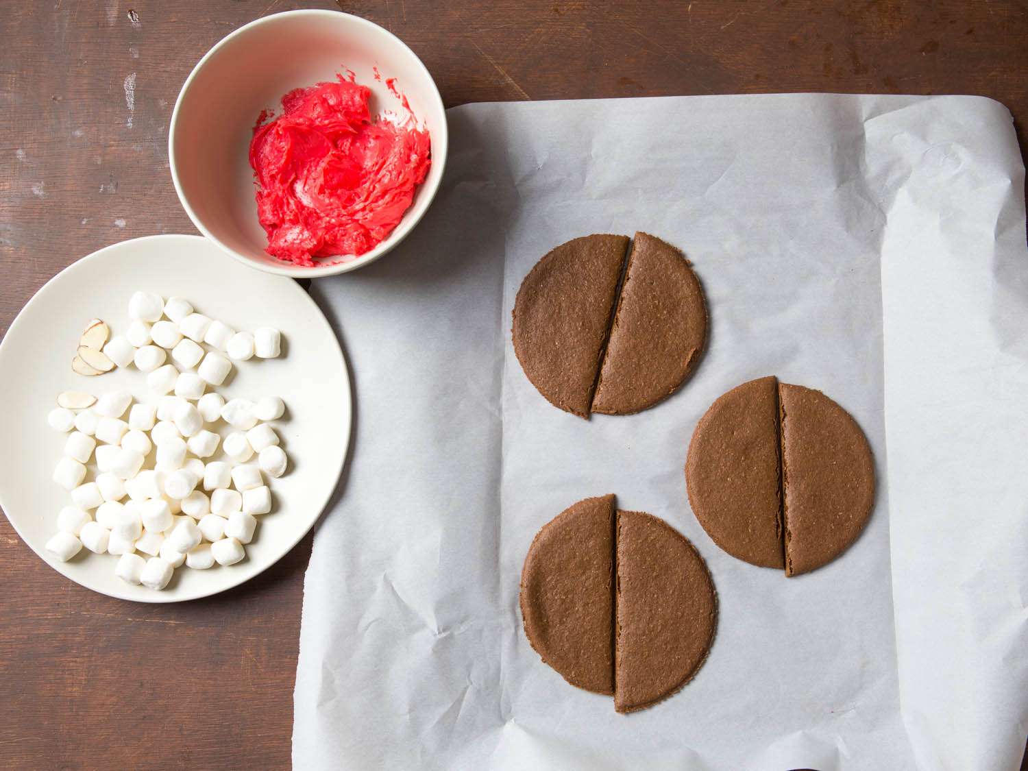 Overhead shot of mini marshmallows, red cream cheese frosting, and rounds of chocolate graham crackers cut in half.