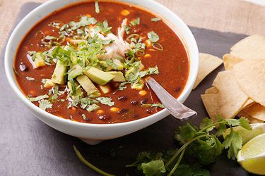 A bowl of tortilla soup with lots of herbs and avocado as garnish.