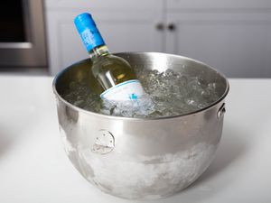 A bottle of wine chilling in heavily iced water in a stainless mixing bowl.