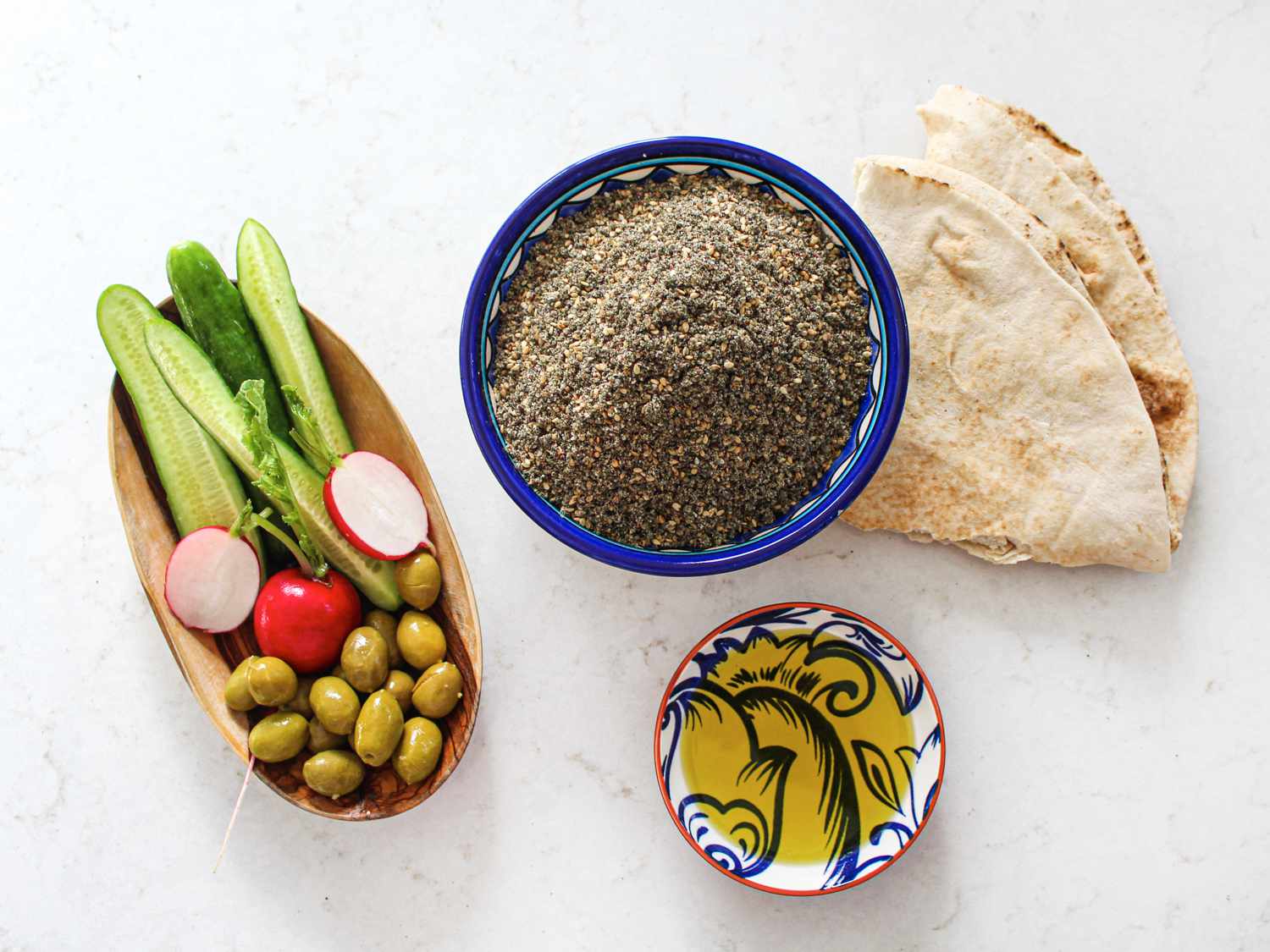 Small bowl of Za'tar next to a piece of pita, a small bowl of olive oil, and a rectangular bowl of vegetables