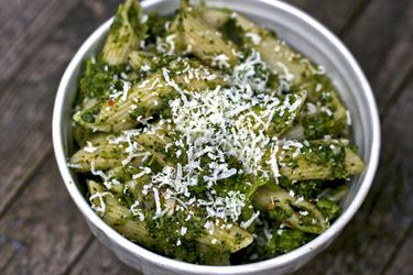 A white dish with pasta e broccoli, with some cheese grated on top.