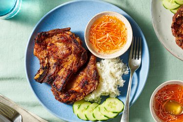 Pork chops over steamed rice white on a plate with sliced cucumbers and a ramekin of sauce