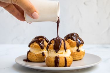 A trio of profiteroles being doused in chocolate sauce