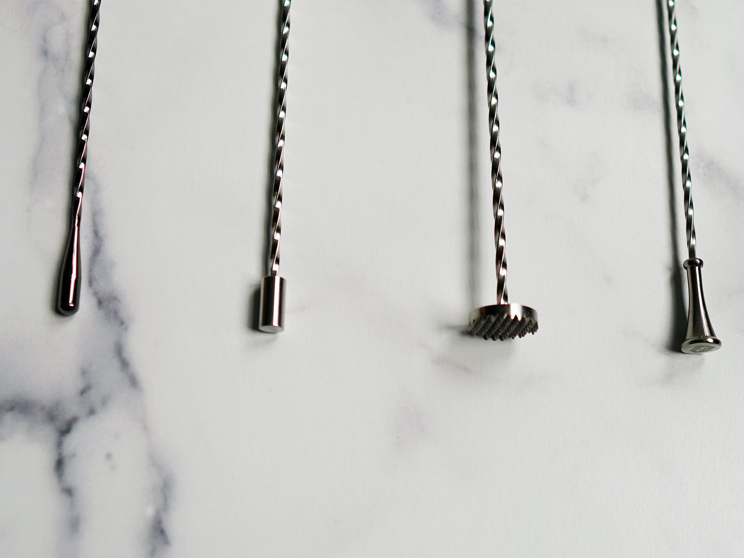 a closeup of the ends of four bar spoons set on a marble surface