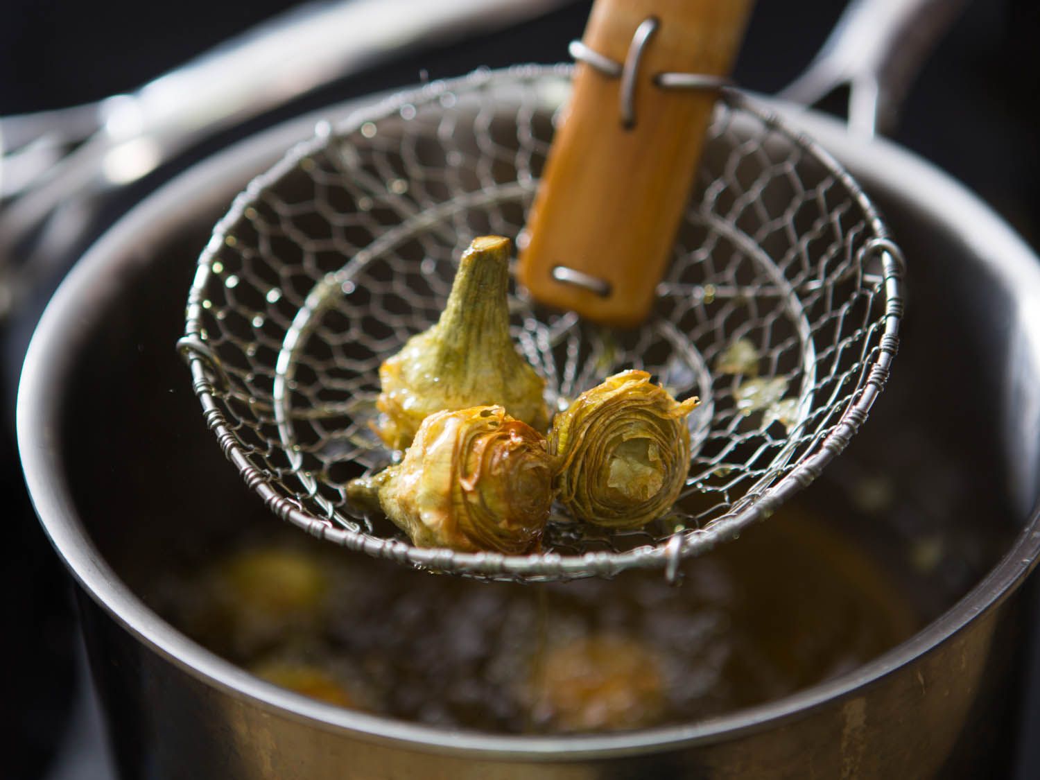 Lifting fried artichoke hearts out of hot oil with spider.