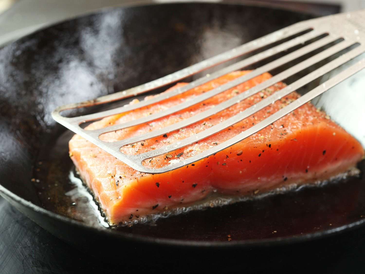 特写一个灵活的开槽铲压在煎锅中的鲑鱼片