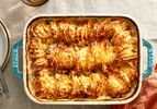 Browned hasselback potatoes in a blue stoneware baking dish on a linen tablecloth.