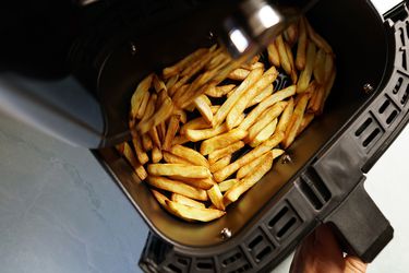 cooked fries in an air fryer basket with a hand pulling the basket out midway