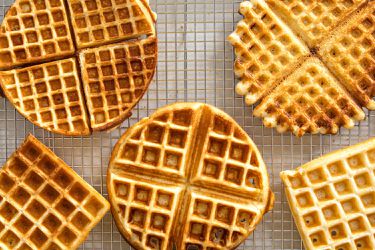 A variety of waffles made with different waffle makers displayed on a wire rack