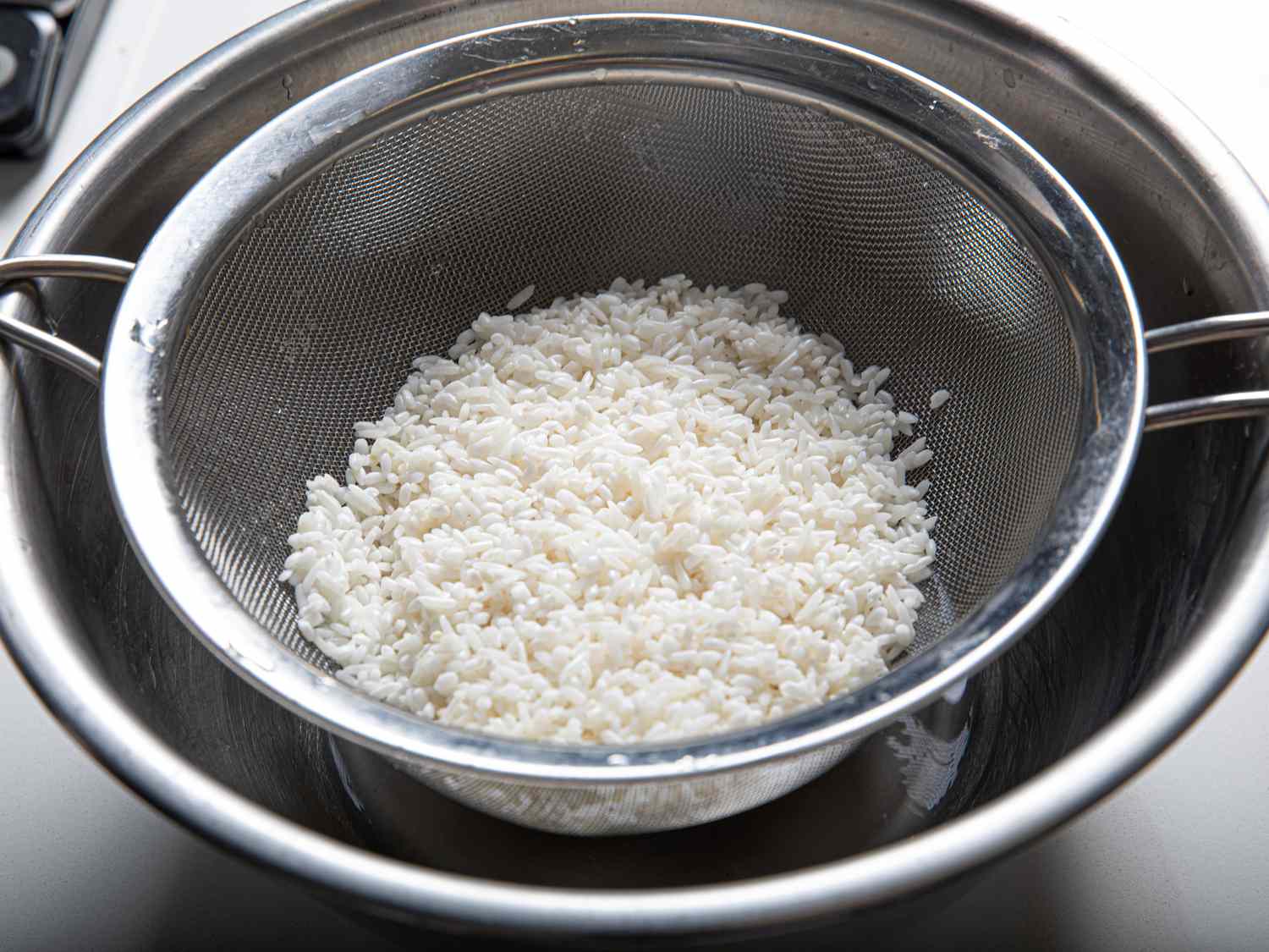 Rice being drained in a fine-mesh strainer set over a bowl.