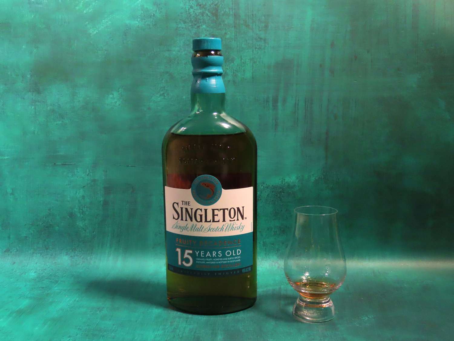 a bottle of singleton on a blue-green surface with a whisky glass beside it