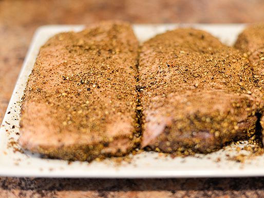 Raw duck breasts covered in ground spices on a white plate