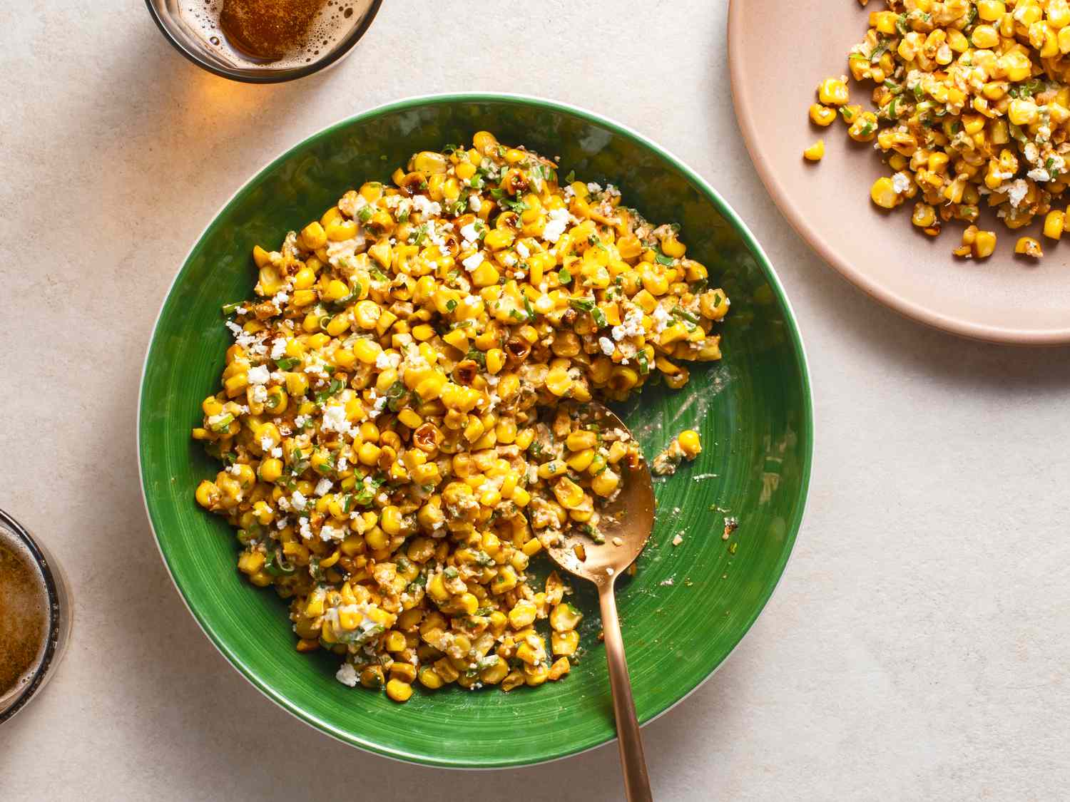 Esquites in a green ceramic bowl with a serving spoon