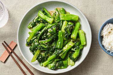 Stir-fried choy sum with minced garlic on a serving platter and a side of Jasmine rice in a small bowl