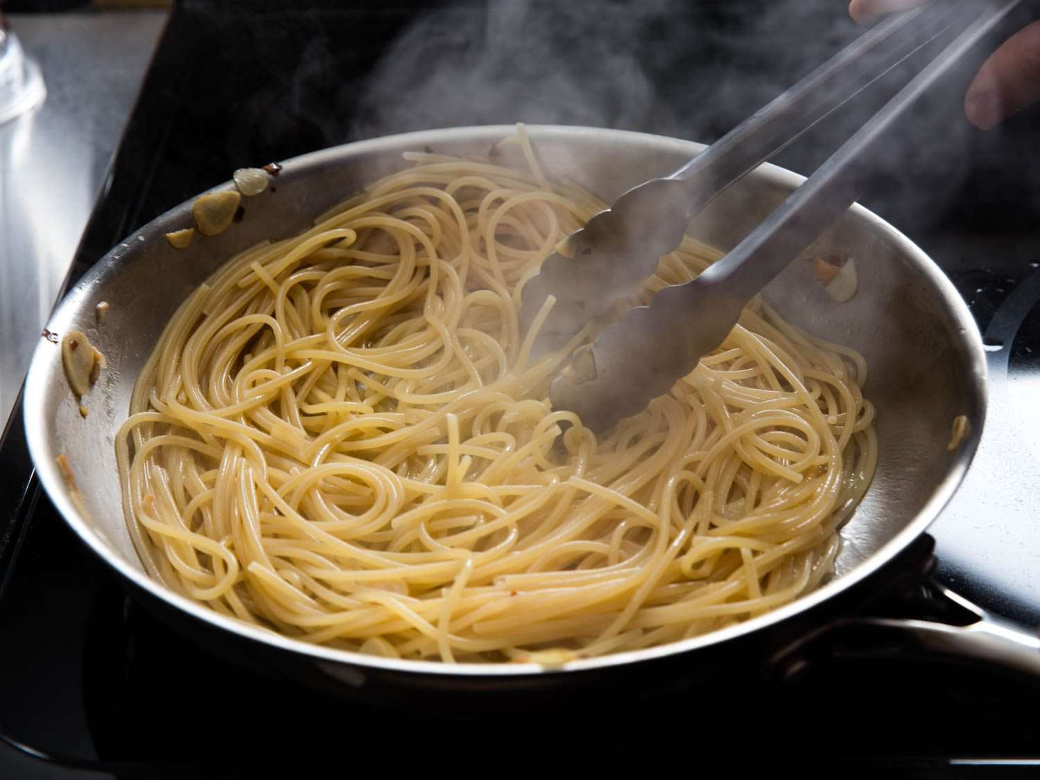 Spaghetti is finished in a skillet with some cooking water to make pasta aglio e olio.