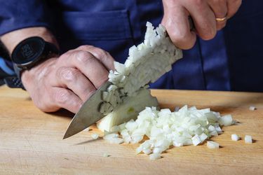 Two hands dicing an onion on a wooden cutting board