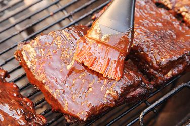 Brushing barbecue sauce on top of ribs on the grill
