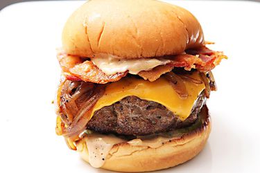 Closeup of an ultimate bacon cheeseburger set on a white surface.