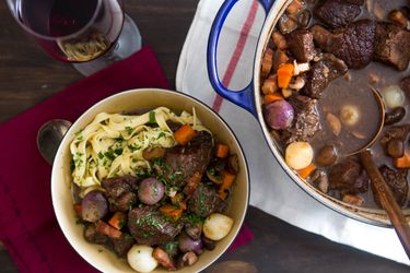 A bowl of Boeuf Bourguignon and noodles next to the pot