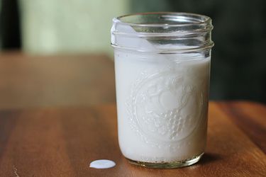 A open mason jar of DIY cultured buttermilk with a little spilled on the table