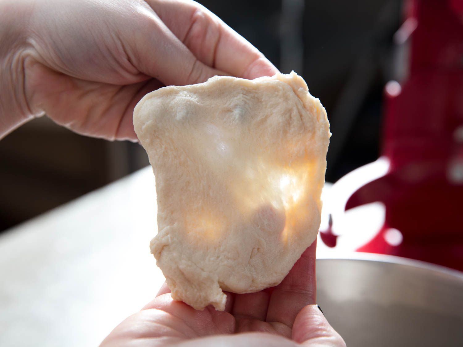 Stretching a small piece of cinnamon roll dough into a thin sheet between fingers for the windowpane test.