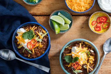 Two bowls of pressure cooker chili topped with cheese, sour cream, cilantro, chile slices, and lime wedges.