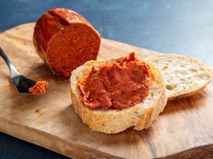 'Nduja next to a slice of bread slathered with 'nduja and a knife on a wooden block.