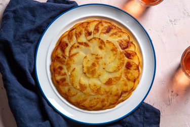 A golden brown pommes anna sits on a serving plate, showing beautiful shingled rounds of thinly sliced potato.