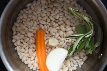 一个装满干豆子、一根胡萝卜、一瓣大蒜、洋葱和一根新鲜鼠尾草的罐子。