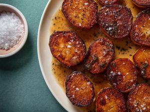 Closeup of a serving platter of fondant potatoes with a ramekin of flaky sea salt on the side.