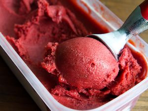 Closeup of plum sorbet being scooped from a container.