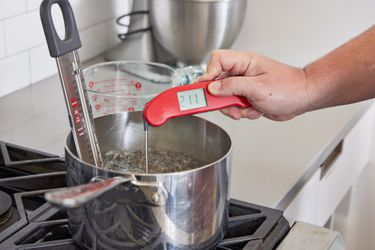 一个hand using an instant-read thermometer to take the temperature of water boiling in a saucepan