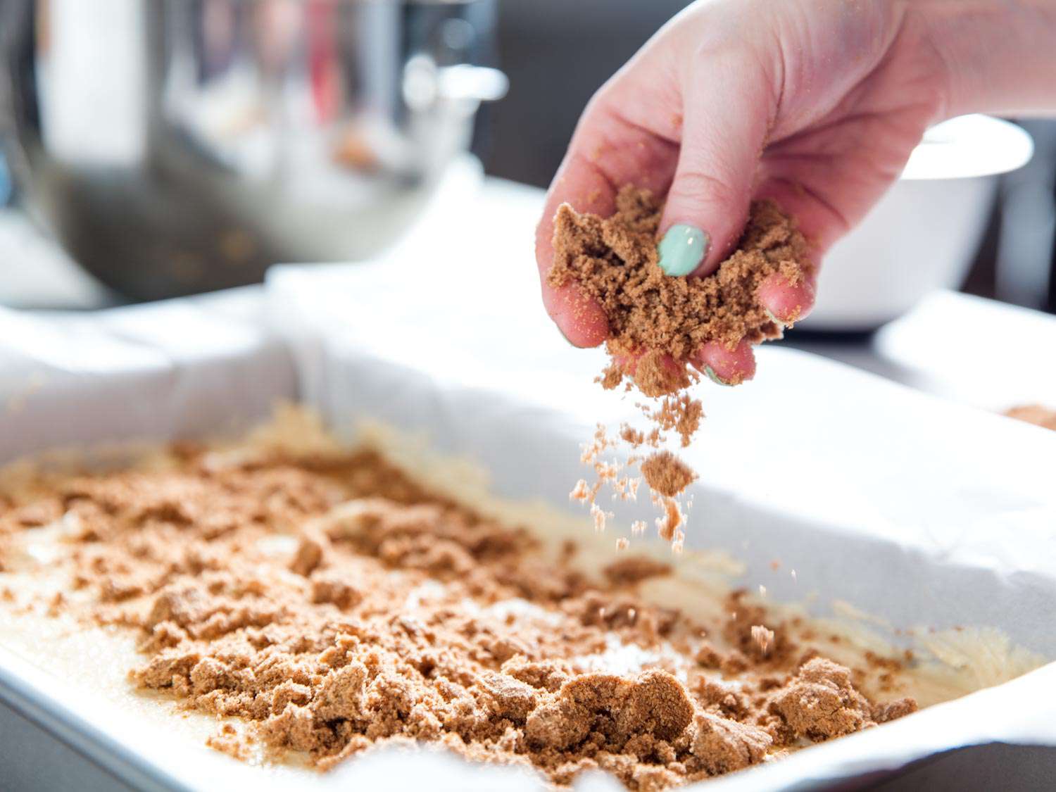 A hand sprinkling crumb topping over batter in a cake pan.