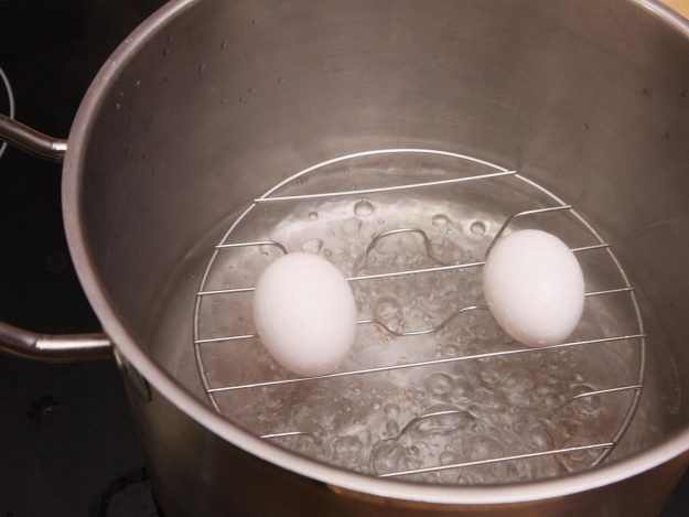 Two eggs resting on top of steamer insert in pot with boiling water.